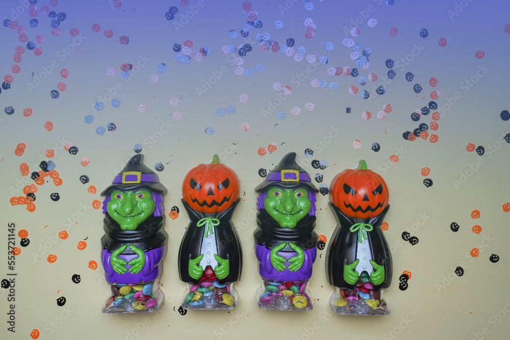 Terrible figures of witches and monsters on a light background strewn with colorful confetti. The concept of the terrible Halloween holiday. Festive figurines.