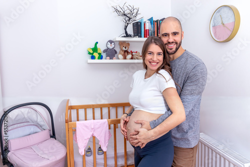 Pregnant woman embraced around her big tummy by her partner. A happy loving couple preparing for childbirth. Looking at camera. photo