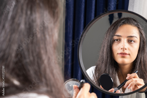 Make up concept, millennial woman sitting at home and doing her own make up concept. Holding tonal powder and brush. Looking to mirror. Fashion and beauty idea image, copy space area for advertisement