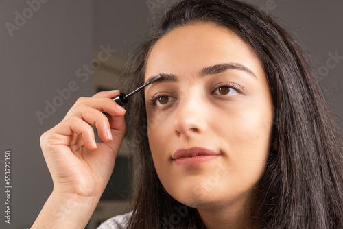Eyebrows brush, beautiful happy girl applying eyebrows brush. Doing her own make up at home. Getting ready for the night. Natural eyebrow correction, beauty concept idea. Perfect soft skin woman.