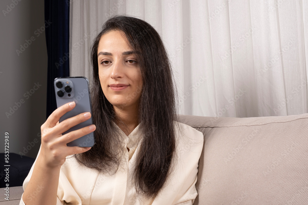 Using modern smartphone, beautiful young caucasian brown haired woman using modern smartphone, cellphone. Sitting at home living room, addiction communication on web, social media, millennial lady.