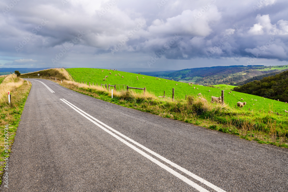 Road through Adelaide Hills farms under stormy clouds during winter season, South Australia