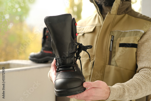 pair black Safety Shoes, work boots made of leather with reinforced cape, high top in hands of young bearded man, builder in uniform, concept of highest product quality, professional workwear photo