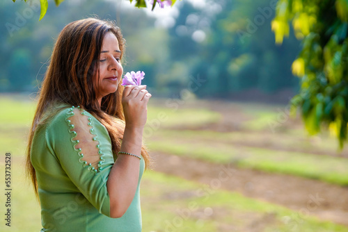 Beautiful young woman smelling flower at park