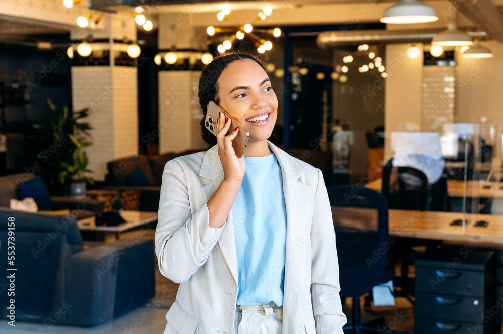 Successful business lady have smartphone conversation with a client, standing in the office, solving work issues, arranging a meeting, looking away, smiling friendly. Mobile phone conversation