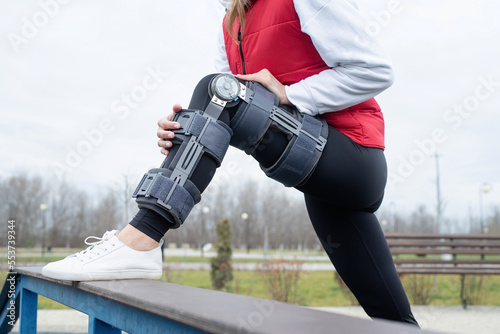 Obraz na plátně Woman wearing knee brace or orthosis after leg surgery working out in the park