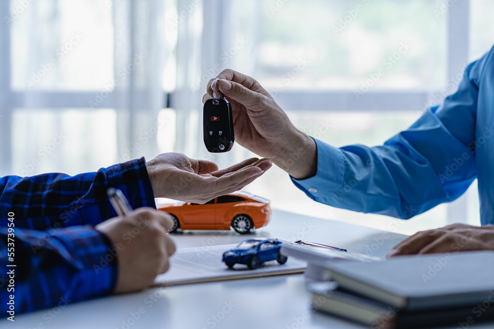 Car salesman handing keys to new car to young businessman client after