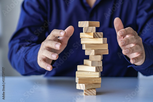 
risk management concepts Hands trying to protect the crumbling wooden blocks block tower businessman carefully placed wooden blocks in tall tower Defending the tall wooden tower was also very risky.
