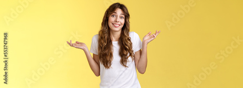 Who cares have fun. Carefree indifferent outgoing happy young woman shrugs raise hands sideways clueless unbothered apathic to topic uninterested smiling broadly careless yellow background photo