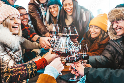 Happy multiracial friends toasting red wine at restaurant terrace - Group of young people wearing winter clothes having fun at outdoors wine bar table