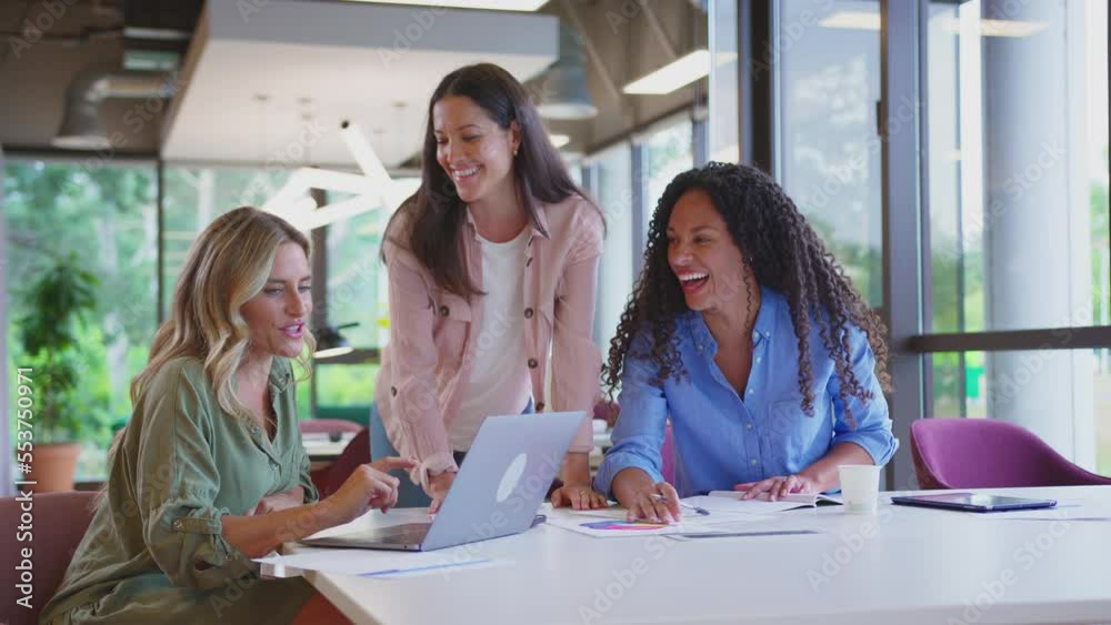 Multi-cultural female business team meeting sitting at desk in modern office using laptop - shot in slow motion Multi-cultural female business team meeting sitting at desk in modern office using laptop - shot in slow motion