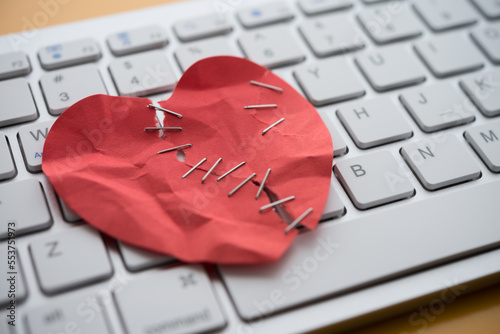 Seriously injured red heart paper with surgical skin stapler on white keyboard computer background. Online internet romance scam or swindler in website application dating concept. Love is bait victim.