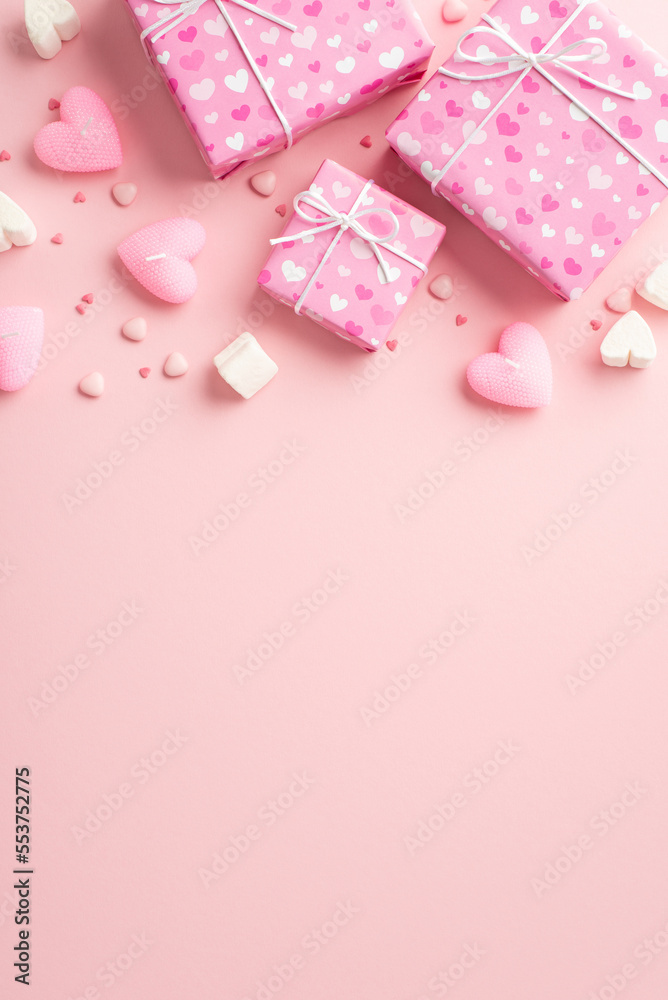 Valentine's Day concept. Top view vertical photo of present boxes in wrapping paper with heart pattern marshmallow candles and sprinkles on isolated pastel pink background with copyspace
