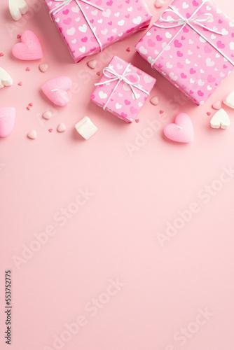 Valentine's Day concept. Top view vertical photo of present boxes in wrapping paper with heart pattern marshmallow candles and sprinkles on isolated pastel pink background with copyspace © ActionGP