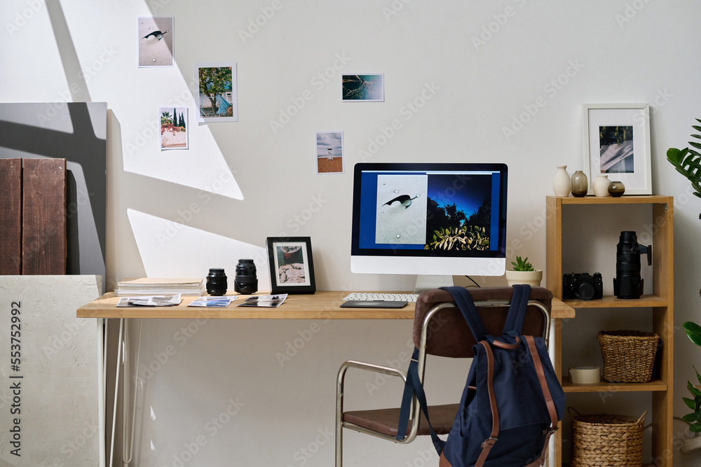 Horizontal image of modern workplace of graphic designer with computer and professional photos on wall in studio