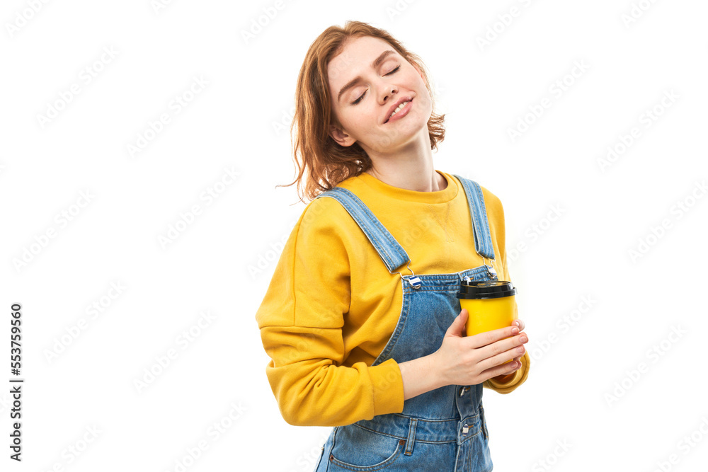 Energetic redhead girl holding and drinking yellow cup of takeaway coffee, smiling and enjoying drink isolated on white background Energetic redhead girl holding and drinking yellow cup of takeaway coffee, smiling and enjoying drink isolated on white background