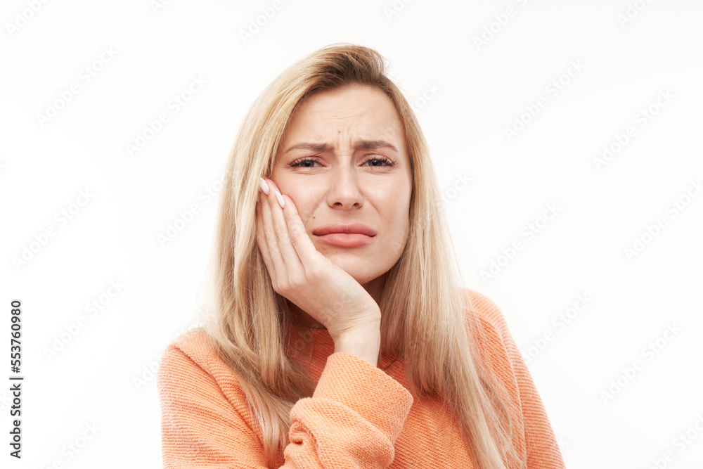 Young blonde woman with suffering face expression holds cheek with hand, touching mouth with palm isolated on white background. Toothache, dental pain concept Young blonde woman with suffering face expression holds cheek with hand, touching mouth with palm isolated on white background. Toothache, dental pain concept