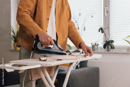 Irons shirt on ironing board, takes care of clothes, housework concept 