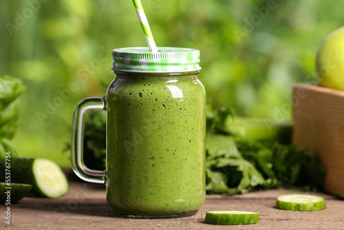 Mason jar of fresh green smoothie and ingredients on wooden table outdoors