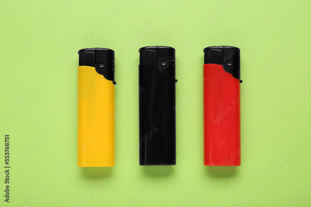 Stylish small pocket lighters on light green background, flat lay Stylish small pocket lighters on light green background, flat lay