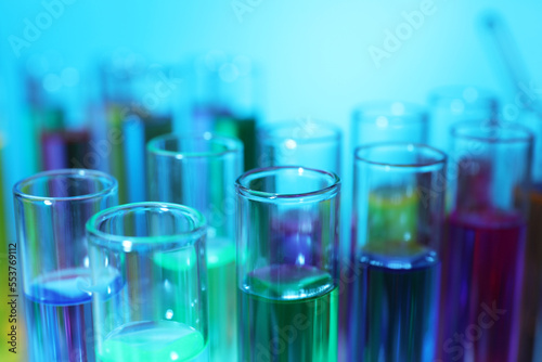 Many test tubes with colorful liquids on light blue background, closeup