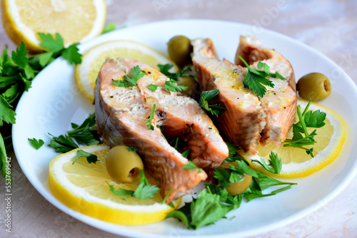 roasted salmon steaks with lemon slices, olives and chopped parsley on plate, macro