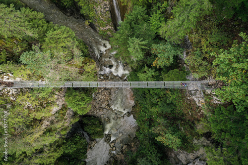 Drone photograph with hiker crossing a suspended metal bridge over a mountain gorge photo