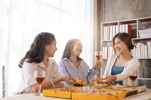 Group of Asian friends gather to celebrate Christmas with champagne and eating pizza at home. Joy of holiday party with friends or colleague concept