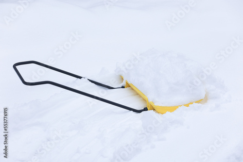 A yellow shovel with snow is lying in a snowdrift. Cleaning tool. Selective focus