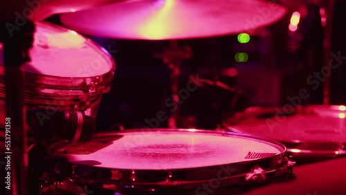 a close-up of a musician actively playing drums and hi-hat, illuminated by pink-red light. The concept of a rehearsal, a concert photo