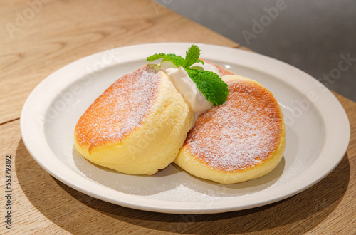 Japanese style sluffy souffle pancake dessert with cream served on a white plate on a wooden table photo