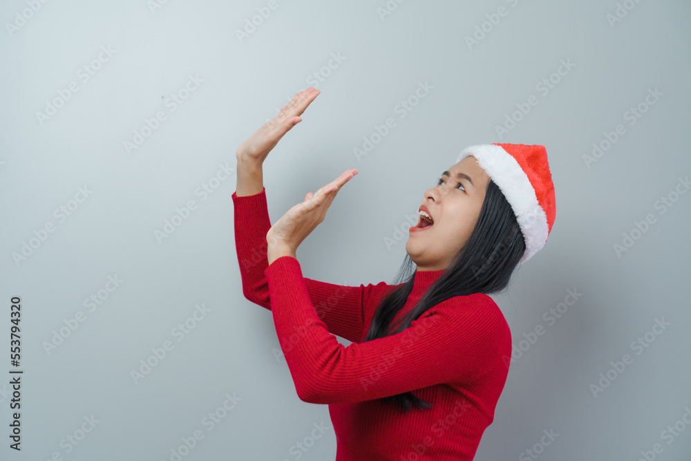 Pretty lovely lady asian thai women in red sweater and santa christmas hat isolated over grey background. wow or surprise