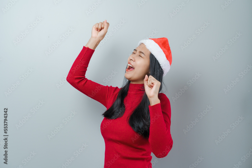 Pretty lovely lady asian thai women in red sweater and santa christmas hat isolated over grey background. dancing