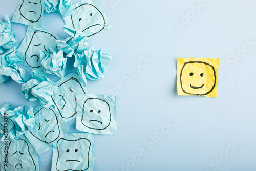 A sad face watching smiling faces from afar. Happy and sad faces drawn on blue stickers. Concepts of exclusion, difference, jealousy.