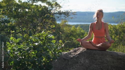 Woman is practicing yoga sitting lotus pose, at a beautiful exotic place on the top of a mountain at sunset. Meditation