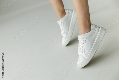 cropped view of woman in white leather sneakers standing on tiptoes on grey background.