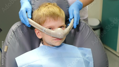 Dentist using nitrous oxide in dental clinic while treating young patients with milk teeth. Relaxation of patient before surgical or dental procedures. Child lying in dental chair with inhalation