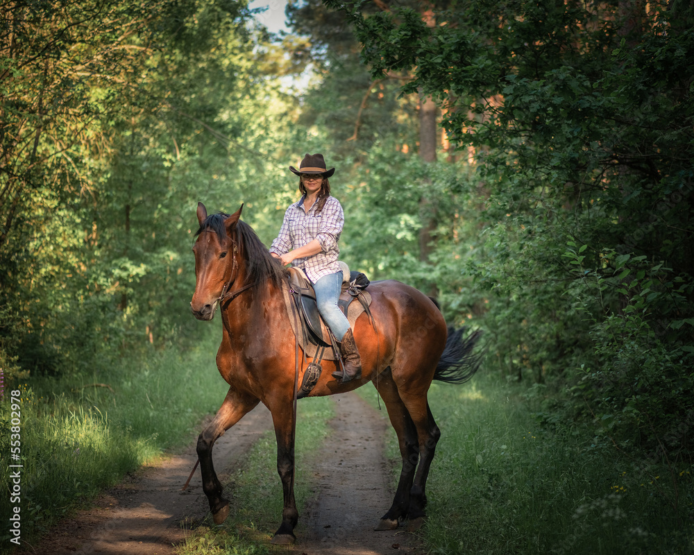 Fototapeta premium Portrait of a young beautiful girl in a cowboy hat on a horse in the forest.