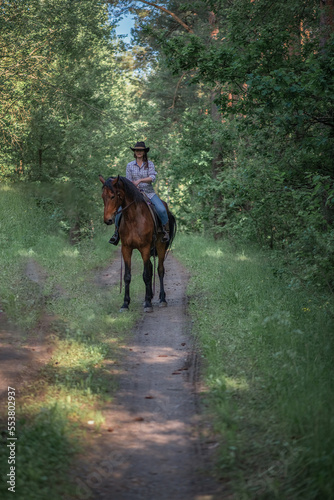 Portrait of a young beautiful girl in a cowboy hat on a horse in the forest. © shymar27
