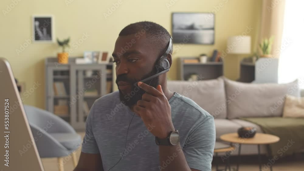 African American male call centre worker using headset microphone while talking to clients, working from home