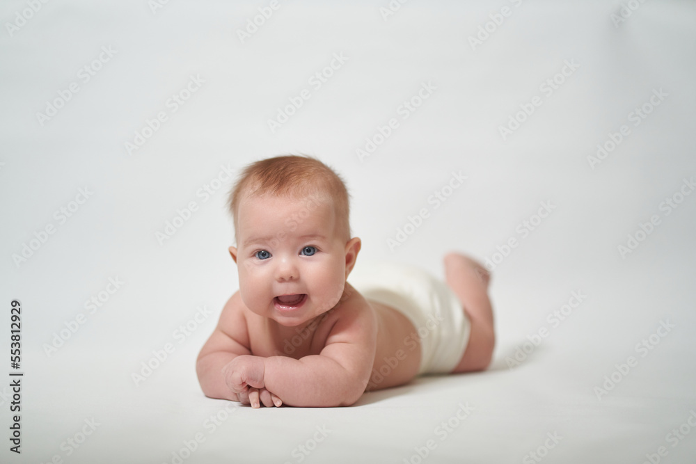 The baby is lying on his belly smiling and looking at the camera with his mouth open against a white background. The baby is lying on his belly smiling and looking at the camera with his mouth open against a white background.