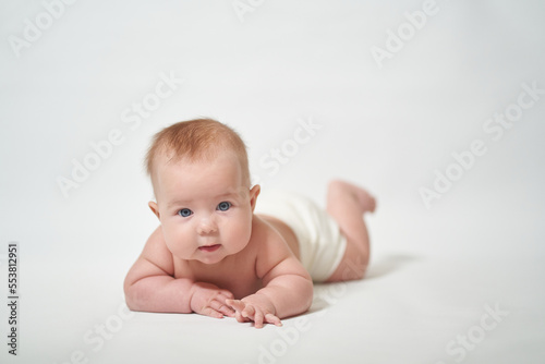 baby lying on his belly looking at the camera with interest against a white background