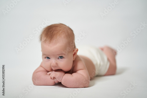 Infant lying on his belly licking his fingers against a white background