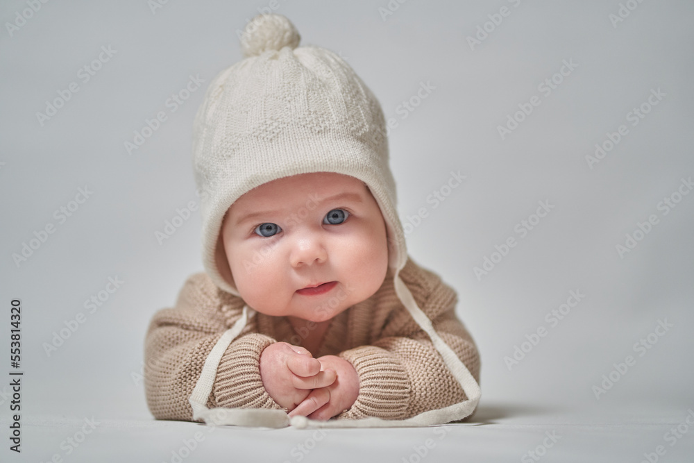 A portrait of an infant in knitted clothes and a white cap looks at the camera A portrait of an infant in knitted clothes and a white cap looks at the camera