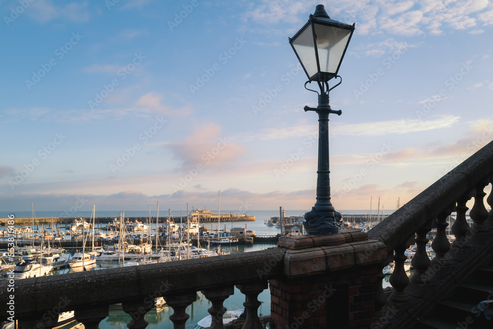 Vintage street lamp along a balustrade wall with a backdrop of Ramsgate Royal Harbour in late afternoon sunshine.