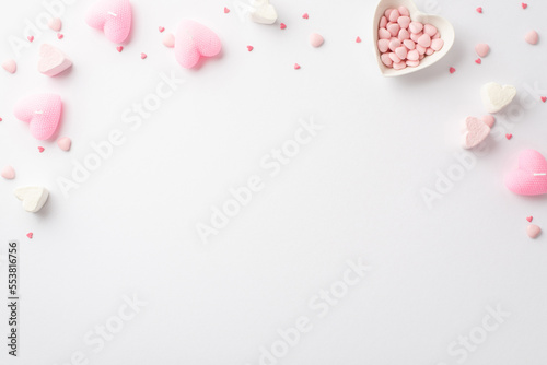 Saint Valentine's Day concept. Top view photo of heart shaped marshmallow pink candles and saucer with sprinkles on isolated white background with copyspace