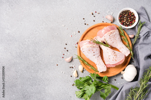 Raw chicken drumsticks with seasonings on wooden plate over gray concrete table. Chicken legs ready to cook. Organic meat, healthy eating concept, copy space