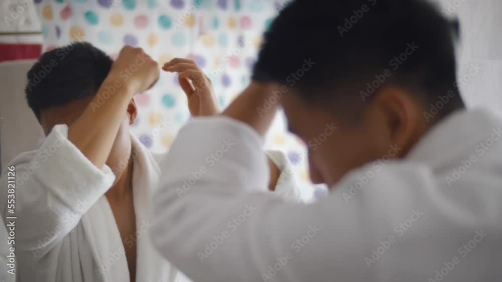 Mirror reflection asian handsome man styling hair with comb in bathrobe. Realtime Mirror reflection asian handsome man styling hair with comb in bathrobe. Realtime