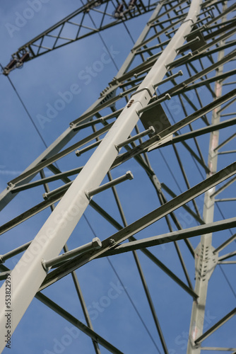 Konzept Energie und Stromversorgung: Detail eines Freileitungsmastes mit Isolationsketten und Schwingungsdämpfern vor blauem Himmel, Hochformat