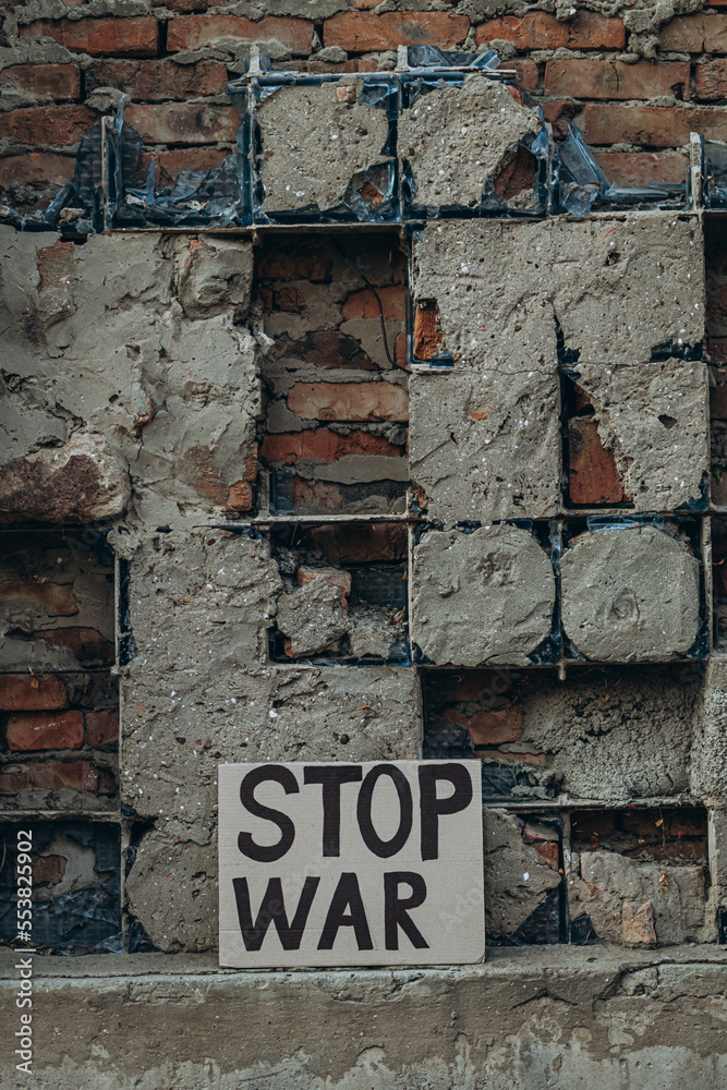 Naklejka premium Ukrainian protest against war with banner placard with inscription message text STOP WAR, ruined city background. Crisis, peace, Russian aggression invasion concept. anti-war demonstration.